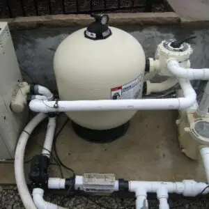 Pool equipment on a concrete pad including a round tan sand filter, pump, and PVC piping.