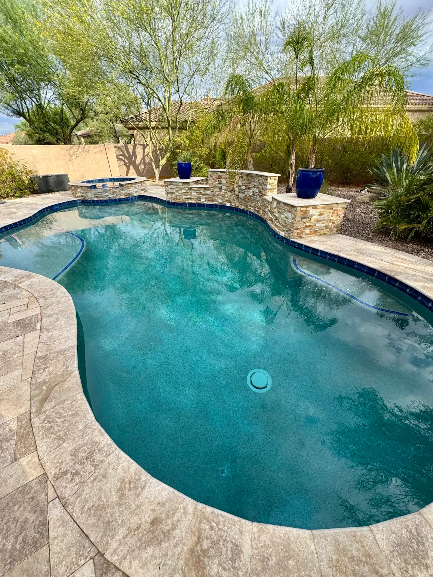 Freeform backyard pool with a travertine deck and a raised stone spa wall