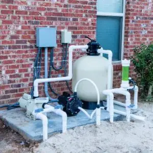 Sand filter, pump and plumbing on an equipment pad against a brick wall