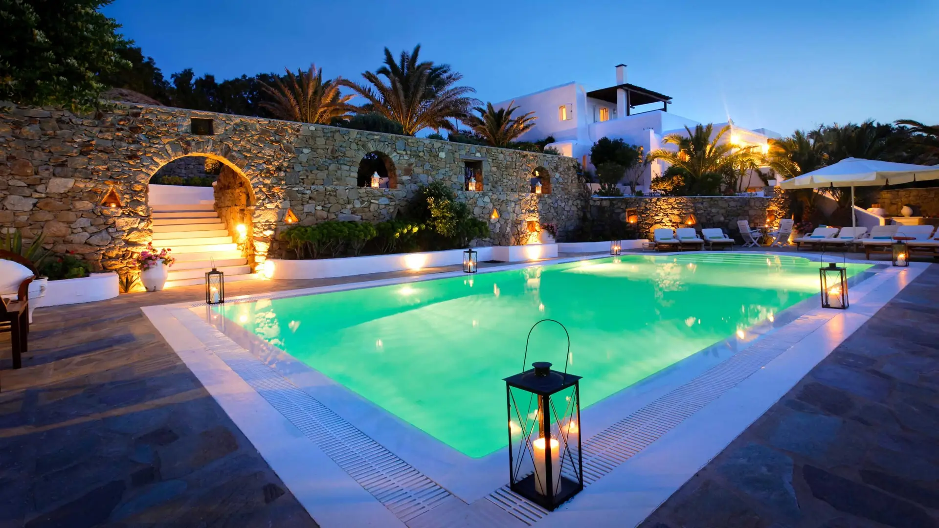LED pool lights glowing in a pool at dusk with lanterns on the deck
